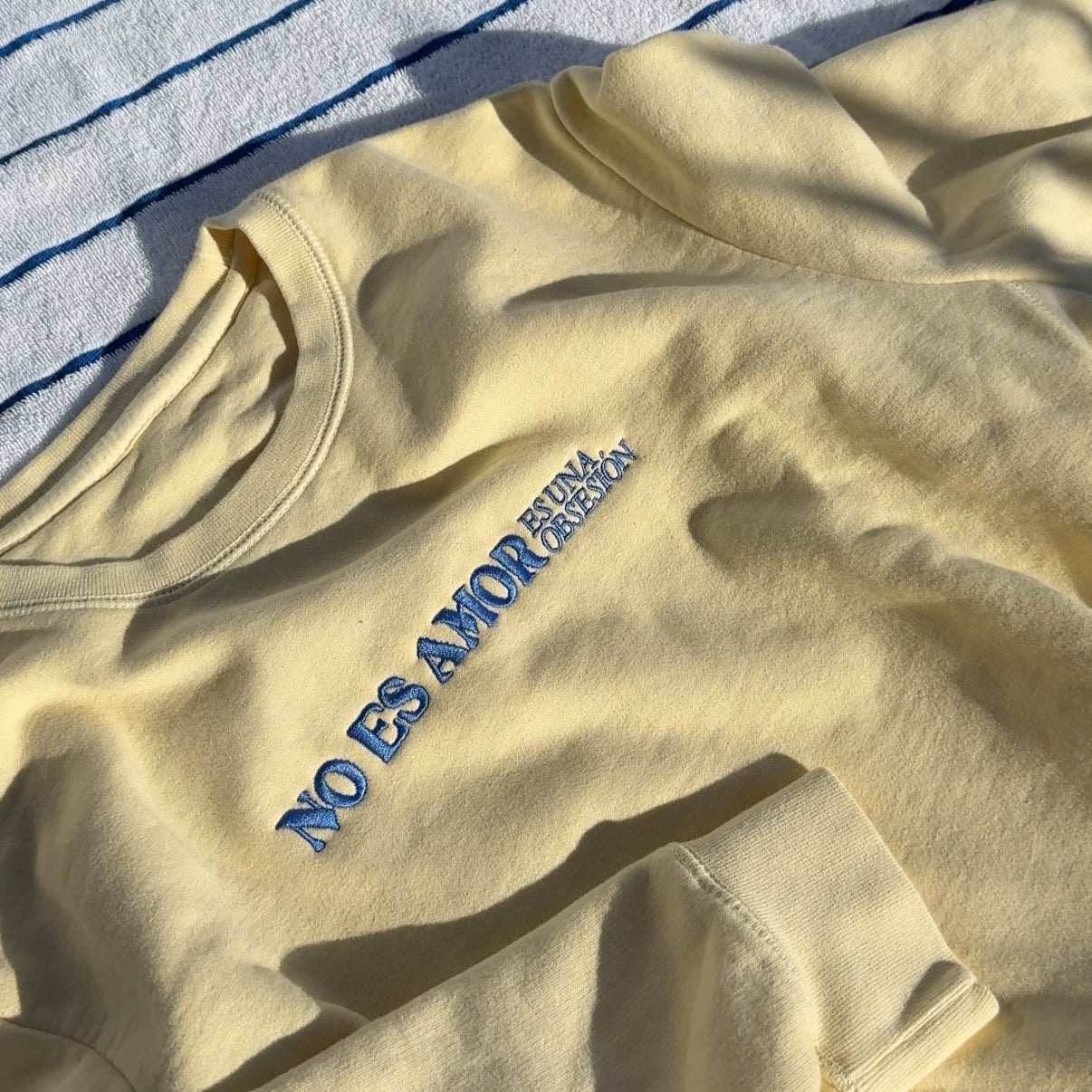 butter yellow sweatshirt with blue embroidered text on a striped fabric background